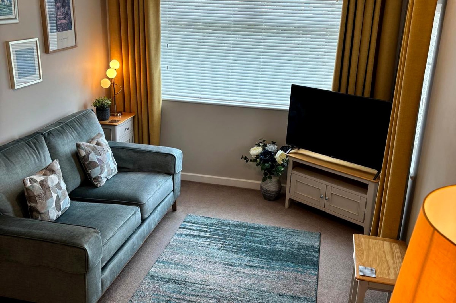 The Bungalow Burnley living room with sofa, armchair, TV and warm lamps